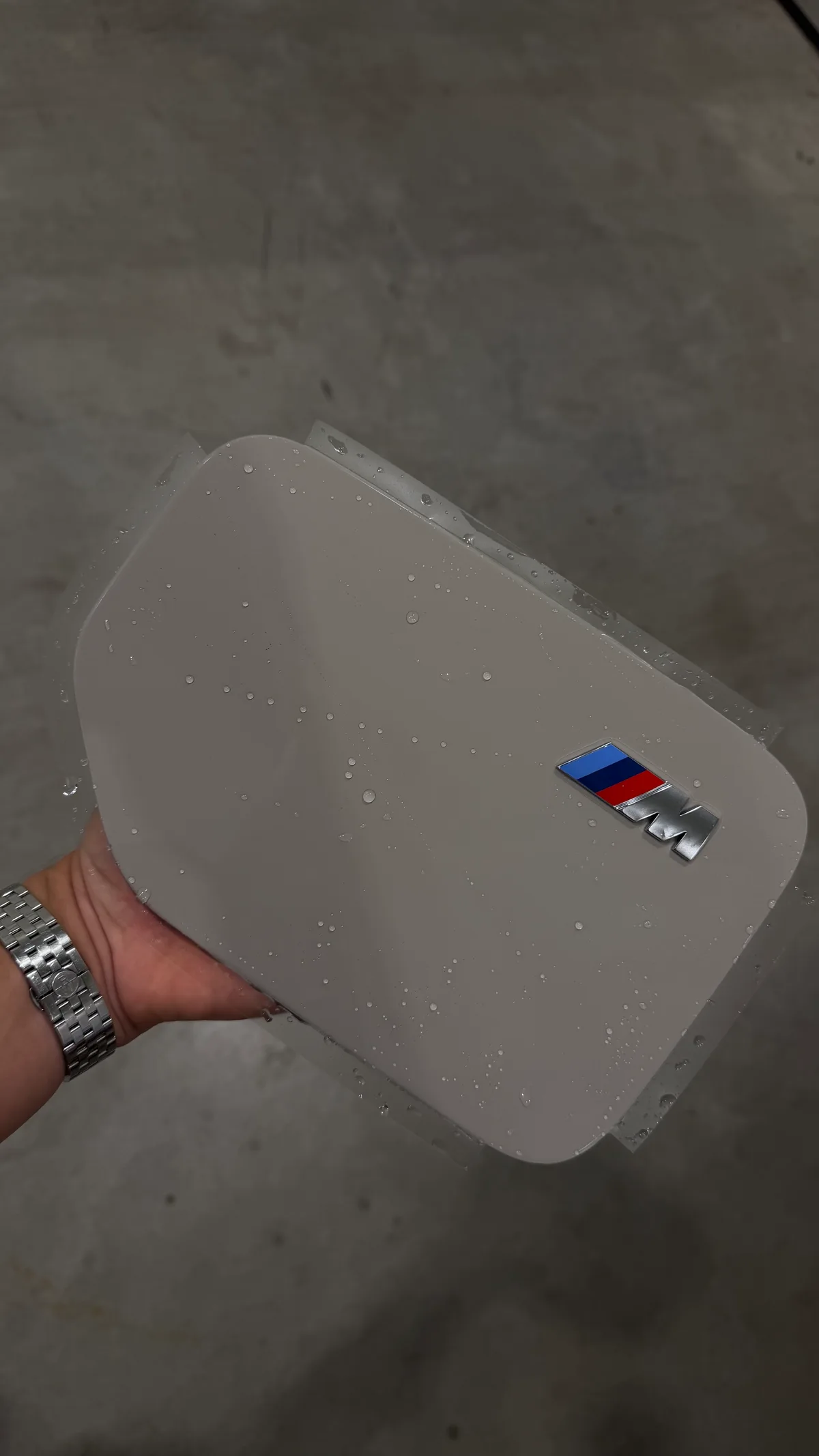 BMW charging cap held in the workshop with wet protection film and a cutout around the M badge.
