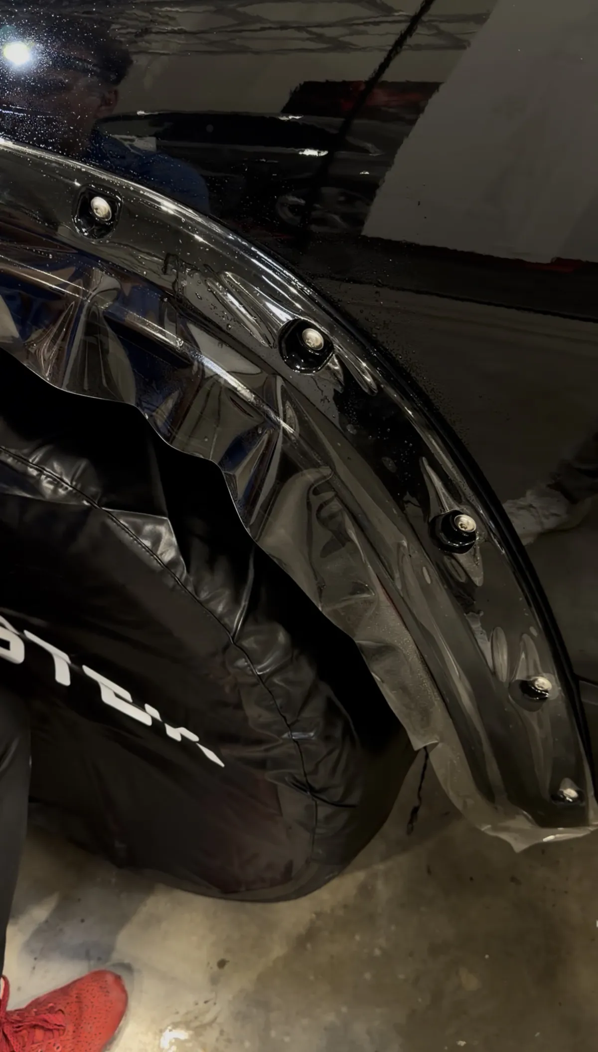 The cut film being laid over the gloss black fender flare, the plotter-cut openings lining up with the bolt pockets.
