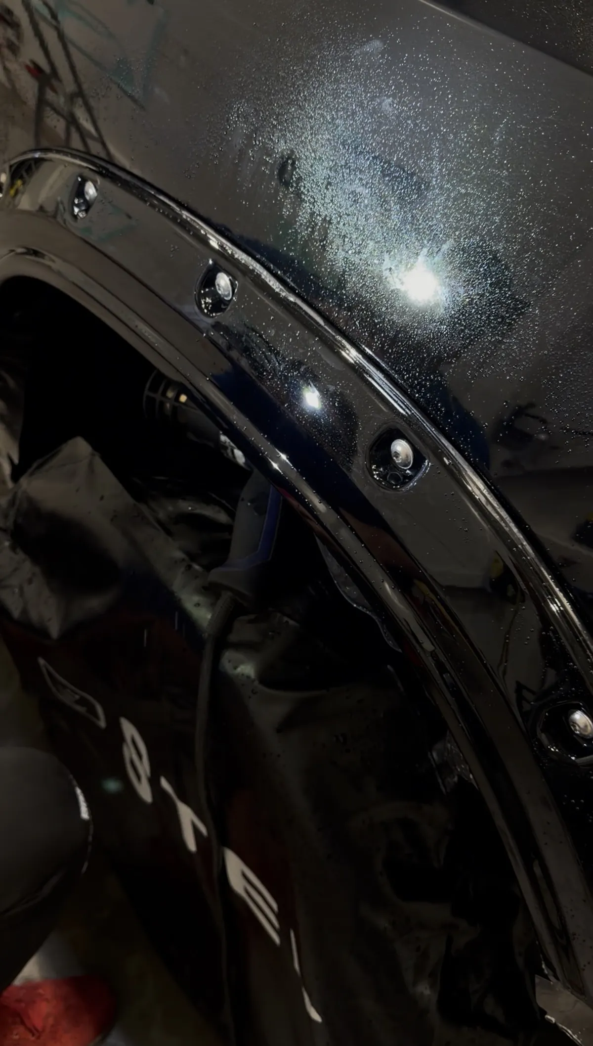 The finished fender flare under paint protection film: gloss black, wet from the install, with a clean opening around every bolt pocket.